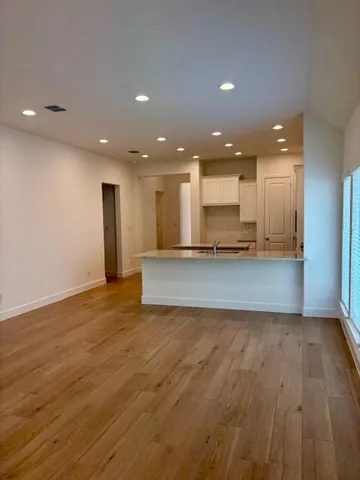 a view of an empty room with kitchen stove window and wooden floor