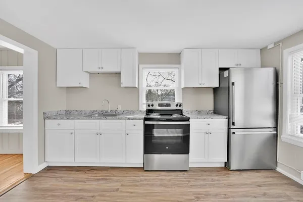 a kitchen with granite countertop a refrigerator stove and white cabinets