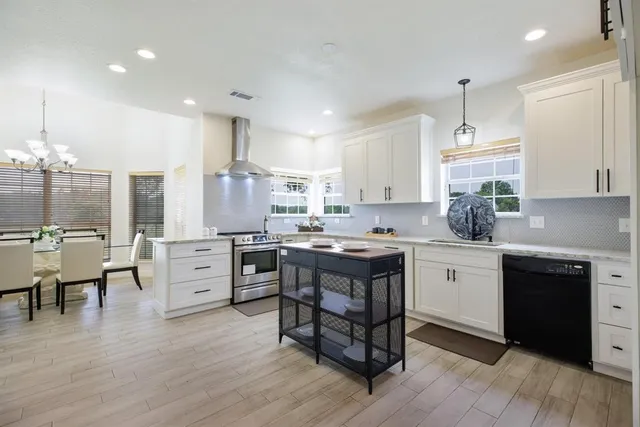 a kitchen with stainless steel appliances granite countertop a refrigerator a sink dishwasher a stove and white countertops with wooden floor