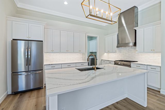 a kitchen with granite countertop a refrigerator a sink dishwasher a stove and white cabinets with wooden floor