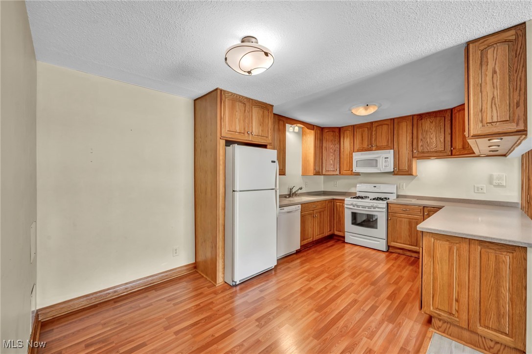 1263 Lost Nation Road, Unit 5 Willoughby, OH 44094 - Photo 11 of 26 Kitchen featuring white appliances, light countertops, a textured ceiling, light wood-style floors, and brown cabinetry