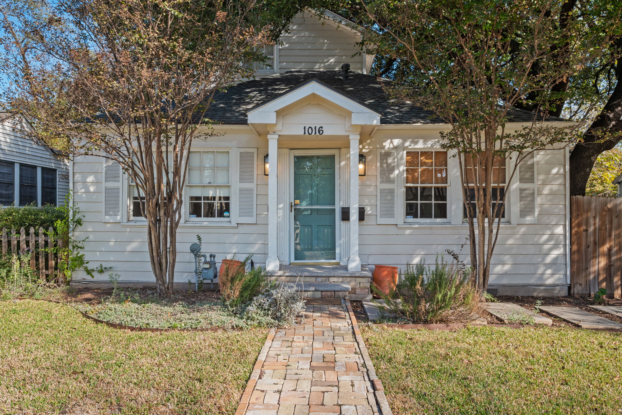 1016 East 43rd Street Austin, TX 78751 - Photo 1 of 1 Charming cottage exterior featuring white siding, a prominent teal entry door, decorative white shutters, and a brick paver walkway