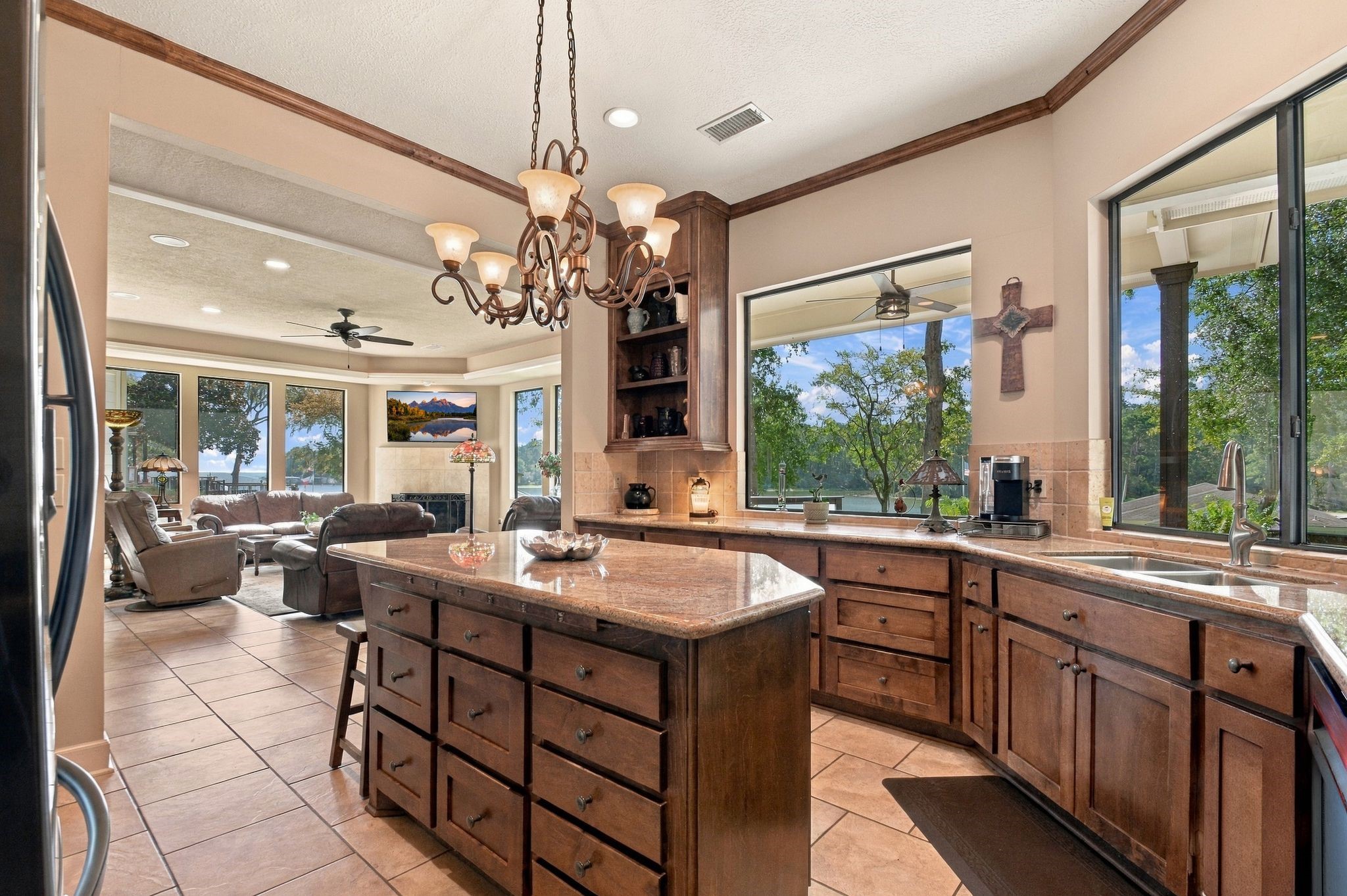 20341 Bay Hill Road Point Blank, TX 77364 - Photo 6 of 50 Spacious kitchen with a large island, rich wooden cabinetry, and expansive windows showcasing stunning outdoor views, seamlessly flowing into a cozy living area with abundant natural light.
