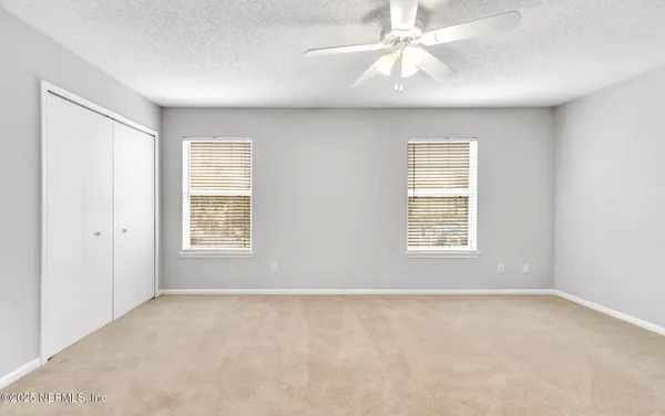 an empty room with chandelier fan and windows