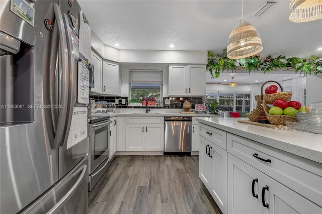 a kitchen with stainless steel appliances granite countertop a stove a sink dishwasher and white cabinets with wooden floor