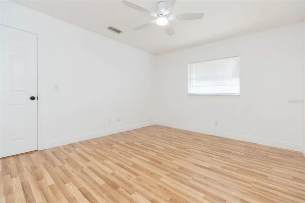 an empty room with wooden floor and fan