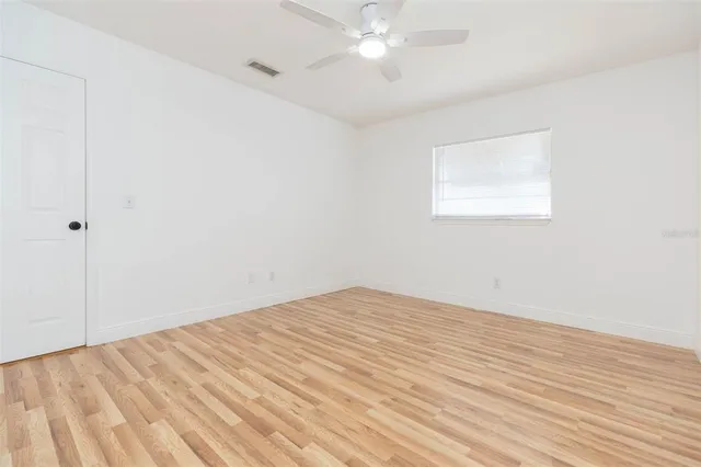an empty room with wooden floor and fan