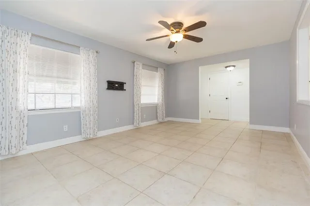 an empty room with chandelier fan and windows
