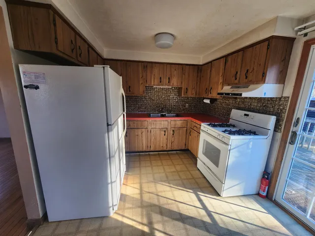 a kitchen with granite countertop a refrigerator a sink a stove and wooden cabinets