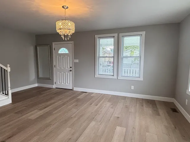 an empty room with wooden floor chandelier and windows