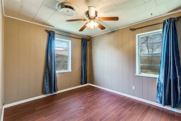 an empty room with wooden floor fan and windows