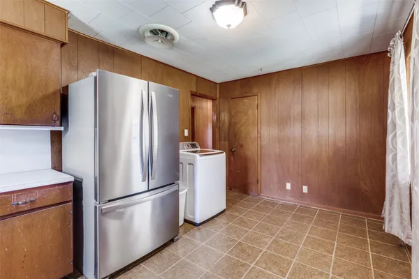 a view of a refrigerator in kitchen and an empty room with wooden floor windows