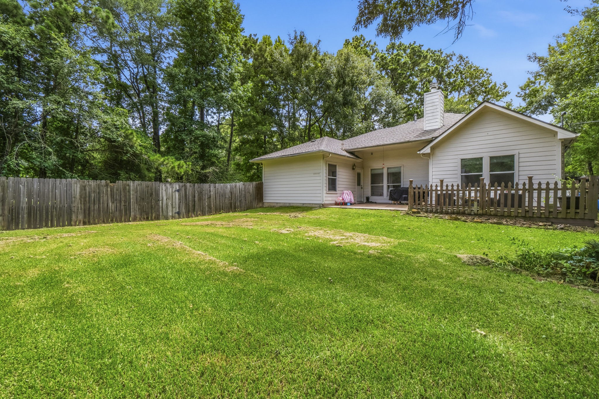 34019 Conroe Huffsmith Road Magnolia, TX 77354 - Photo 17 of 19 This charming home features a spacious, fenced backyard with lush green grass, perfect for outdoor activities. Surrounded by mature trees, it offers privacy and a serene atmosphere. The house has a cozy covered patio for relaxing or entertaining.