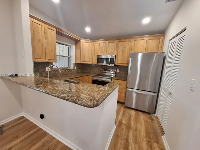 a kitchen with kitchen island granite countertop a refrigerator a sink a stove and white cabinets with wooden floor