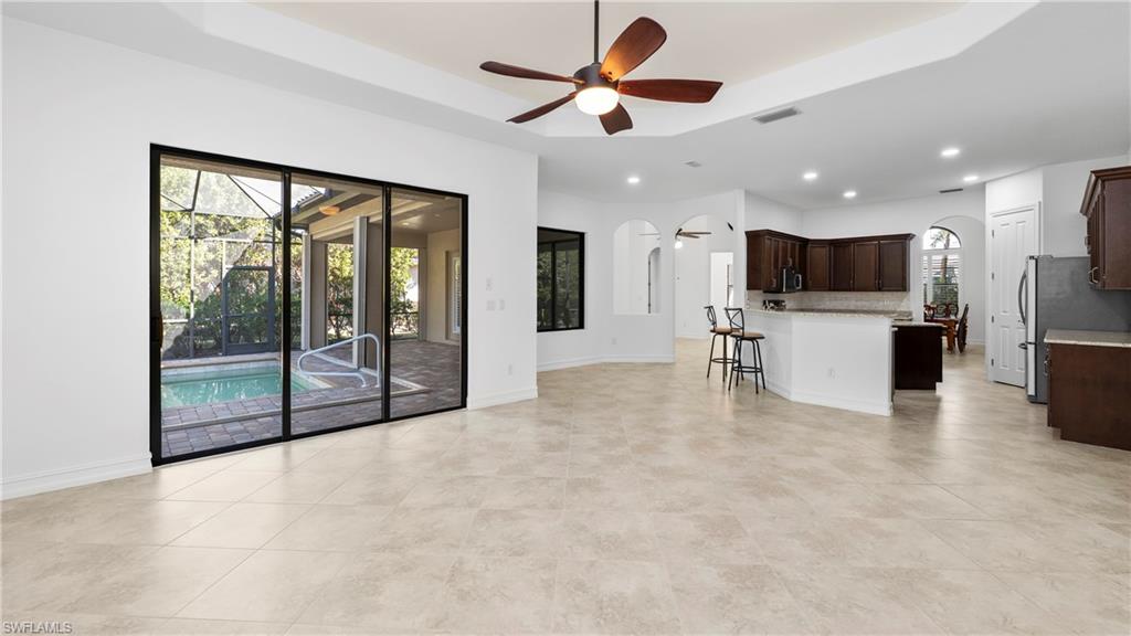 8856 Lely Island Circle Naples, FL 34113 - Photo 13 of 50 Unfurnished living room featuring a ceiling fan, arched walkways, a raised ceiling, a sunroom, and recessed lighting