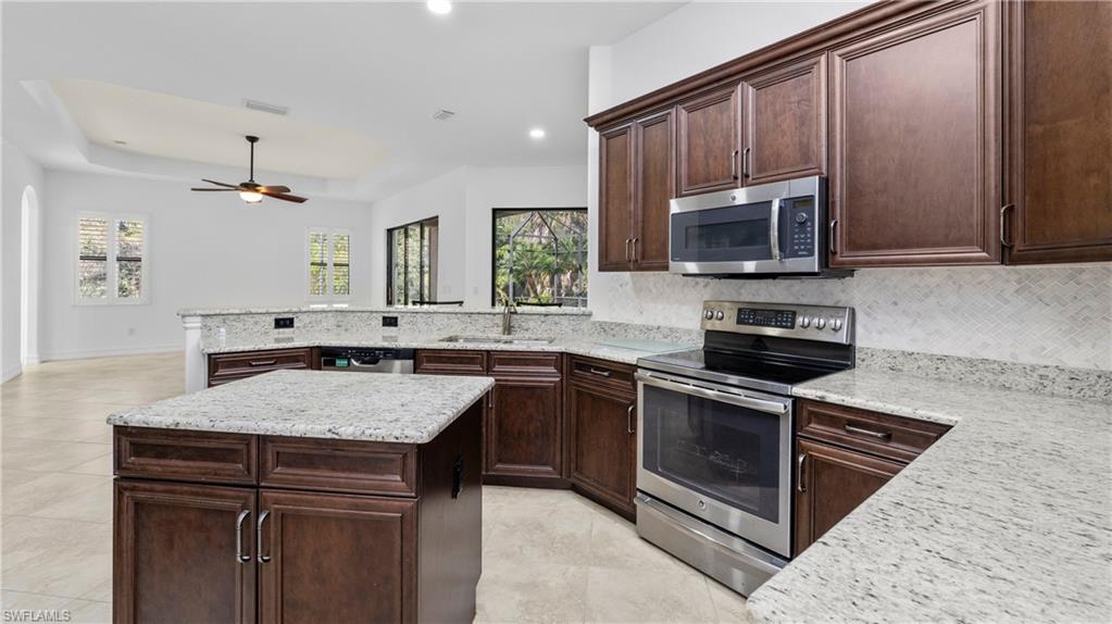 8856 Lely Island Circle Naples, FL 34113 - Photo 14 of 50 Kitchen featuring a raised ceiling, stainless steel appliances, dark wood finish cabinetry, light stone counters, and a peninsula