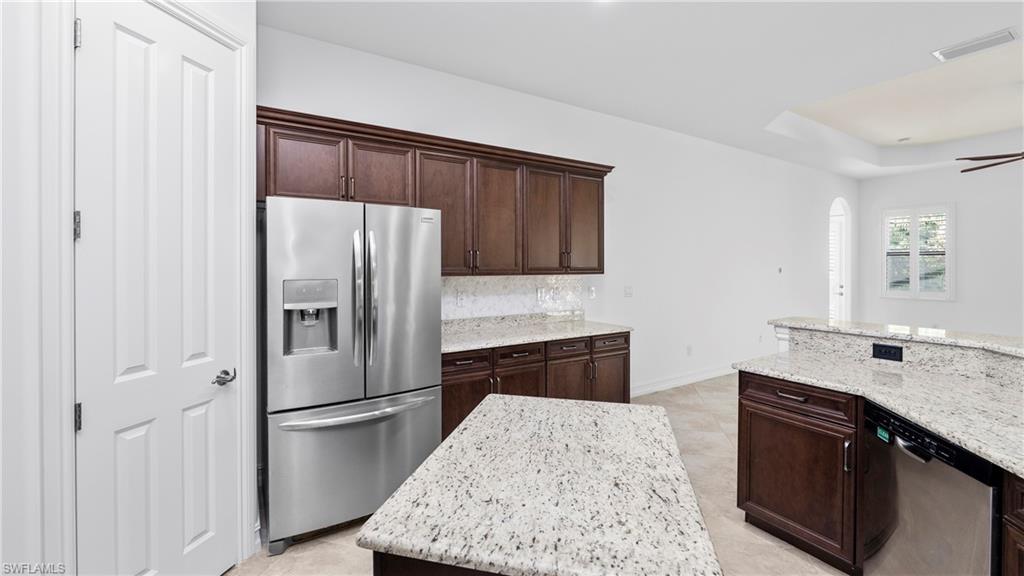 8856 Lely Island Circle Naples, FL 34113 - Photo 15 of 50 Kitchen with stainless steel appliances, light stone countertops, dark wood finish cabinetry, and a kitchen island
