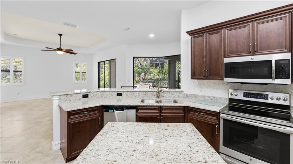 8856 Lely Island Circle Naples, FL 34113 - Photo 15 of 50 Kitchen with dark wood finish cabinets, stainless steel appliances, a peninsula, light stone countertops, and a raised ceiling
