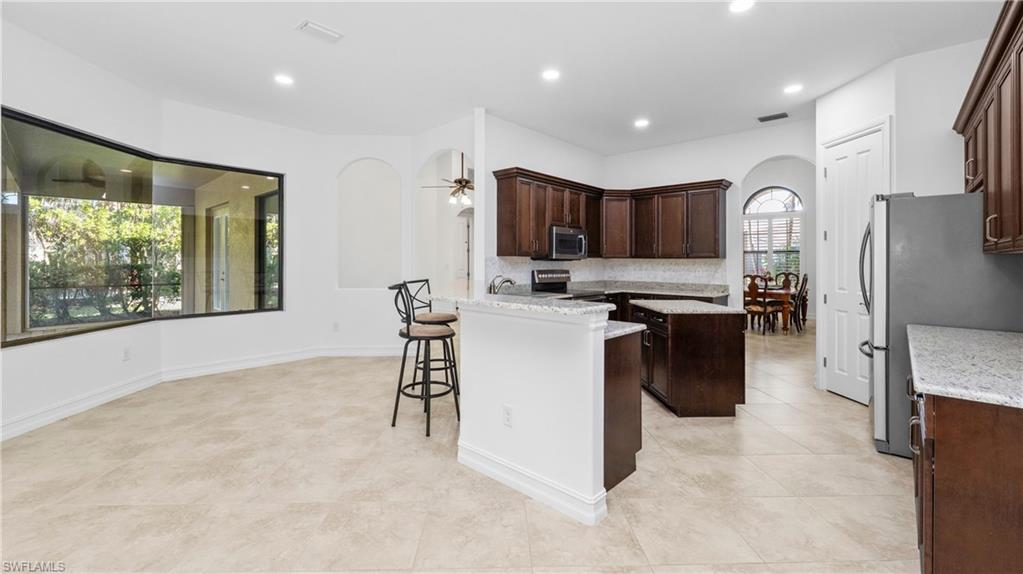 8856 Lely Island Circle Naples, FL 34113 - Photo 18 of 50 Kitchen with arched walkways, dark wood finish cabinets, a center island, light stone counters, and a breakfast bar area