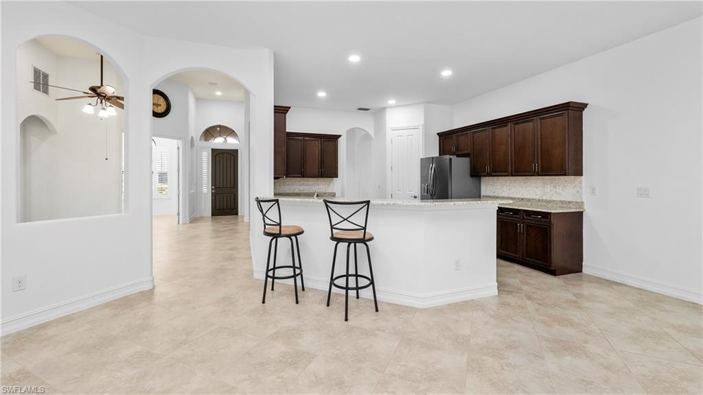 8856 Lely Island Circle Naples, FL 34113 - Photo 19 of 50 Kitchen featuring dark wood finish cabinetry, backsplash, ceiling fan, and arched walkways