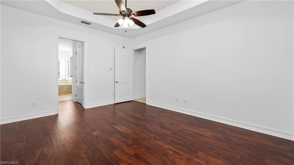 8856 Lely Island Circle Naples, FL 34113 - Photo 23 of 50 Unfurnished bedroom with a raised ceiling, dark wood finished floors, ceiling fan, and ensuite bath