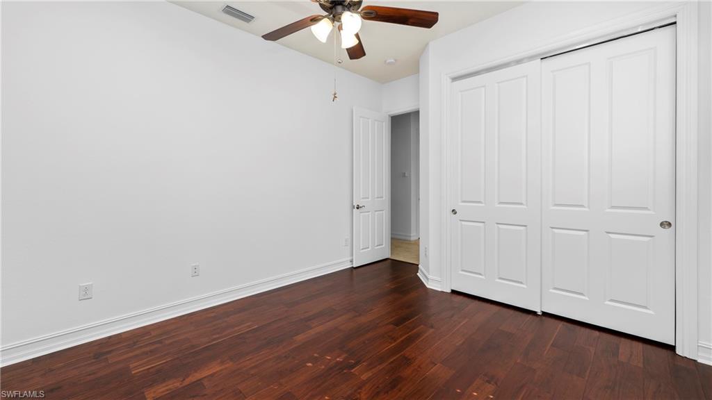 8856 Lely Island Circle Naples, FL 34113 - Photo 28 of 50 Unfurnished bedroom featuring dark wood-style flooring, a ceiling fan, and a closet