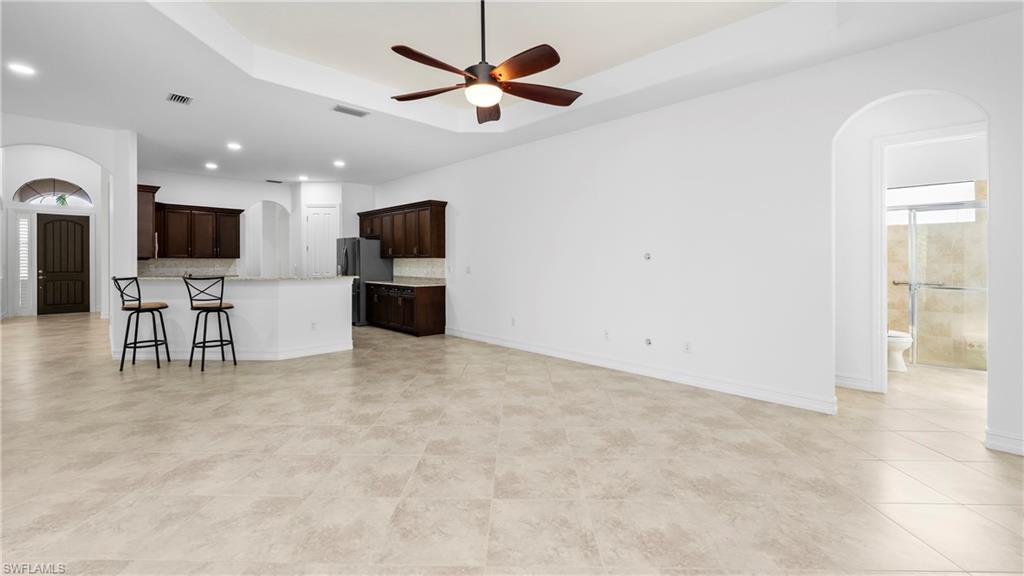 8856 Lely Island Circle Naples, FL 34113 - Photo 10 of 50 Unfurnished living room with arched walkways, a ceiling fan, recessed lighting, and a tray ceiling