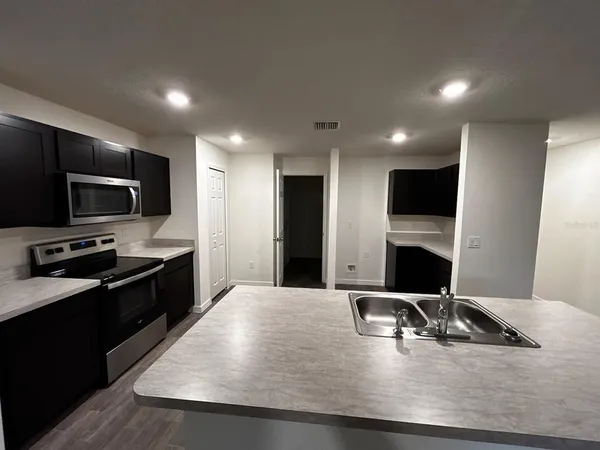 a living room with stainless steel appliances kitchen island granite countertop a sink a stove and a microwave with wooden floor