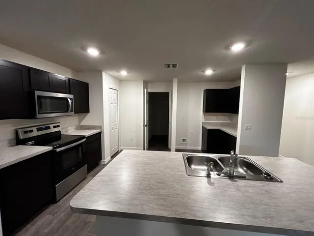 a living room with stainless steel appliances kitchen island granite countertop a sink a stove and a microwave with wooden floor