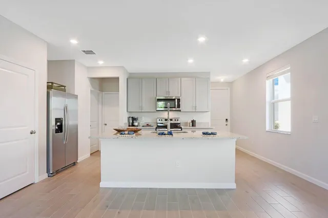 a kitchen with stainless steel appliances a sink a stove a refrigerator cabinets and living room view