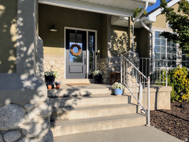 12169 Hidden Valley Road, Unit 44 Sandy, UT 84092 - Photo 7 of 49 Entryway featuring a dark-paneled door with glass inserts, stone-clad columns, stucco exterior, multi-pane windows, and concrete steps with a metal handrail