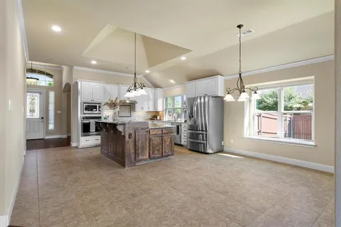 a kitchen with stainless steel appliances kitchen island granite countertop a refrigerator a oven a sink and a large window