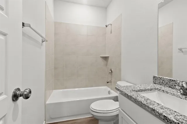 a bathroom with a granite countertop bathtub shower sink vanity mirror and toilet