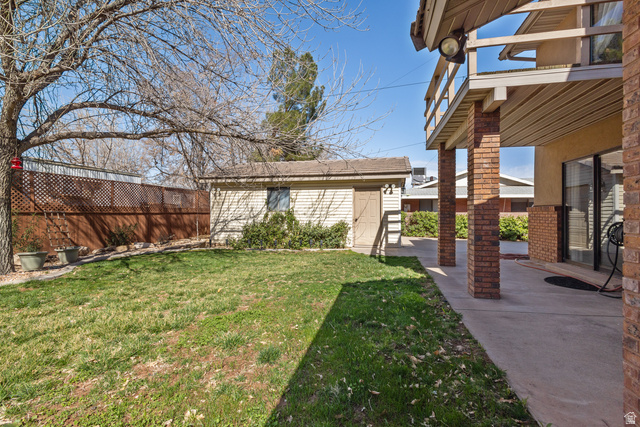 892 Cambridge Drive St. George, UT 84770 - Photo 59 of 65 Expansive backyard featuring a detached storage shed, privacy fencing, and a concrete patio with brick pillars supporting an upper-level balcony