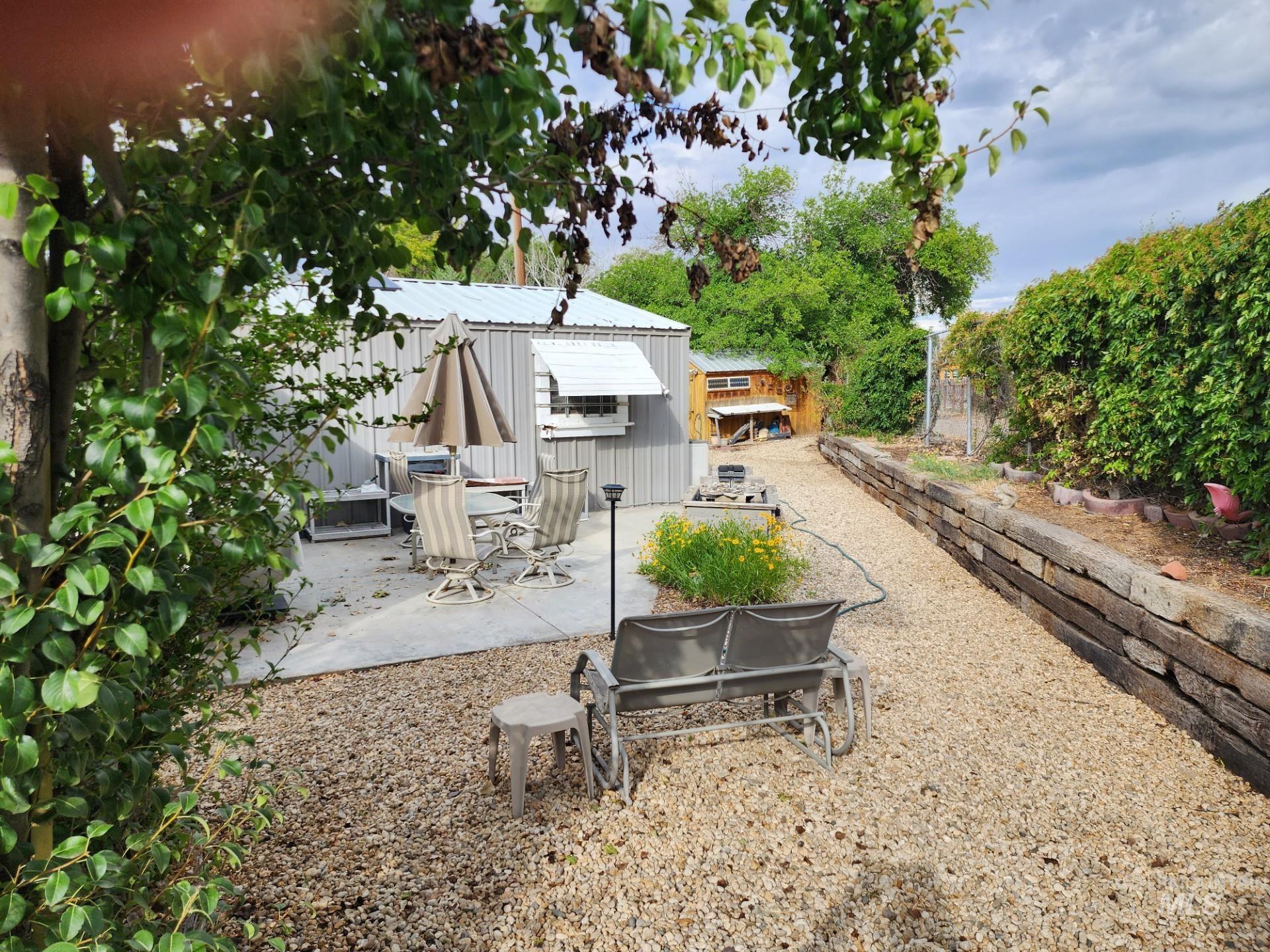 235 5th Street Grand View, ID 83624 - Photo 22 of 22 Backyard area featuring a concrete patio, gravel pathway, wood retaining wall, and mature perimeter foliage