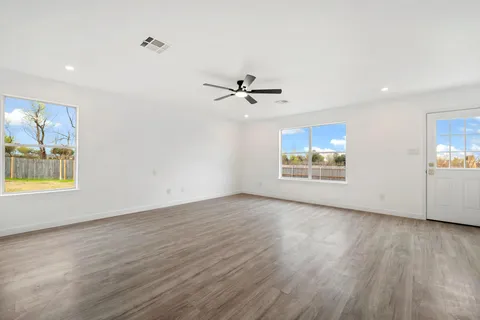 an empty room with wooden floor chandelier fan and windows