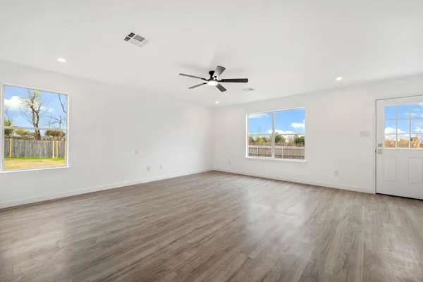 an empty room with wooden floor chandelier fan and windows