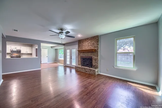 an empty room with wooden floor fireplace and windows