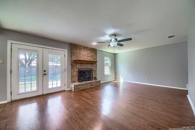 a view of an empty room with wooden floor fireplace and a window