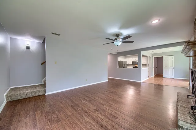 an empty room with wooden floor chandelier fan and windows