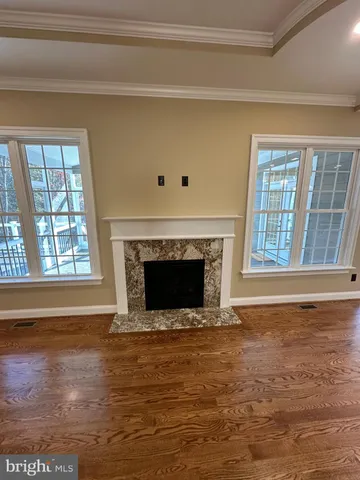 a view of an empty room with wooden floor fireplace and a window
