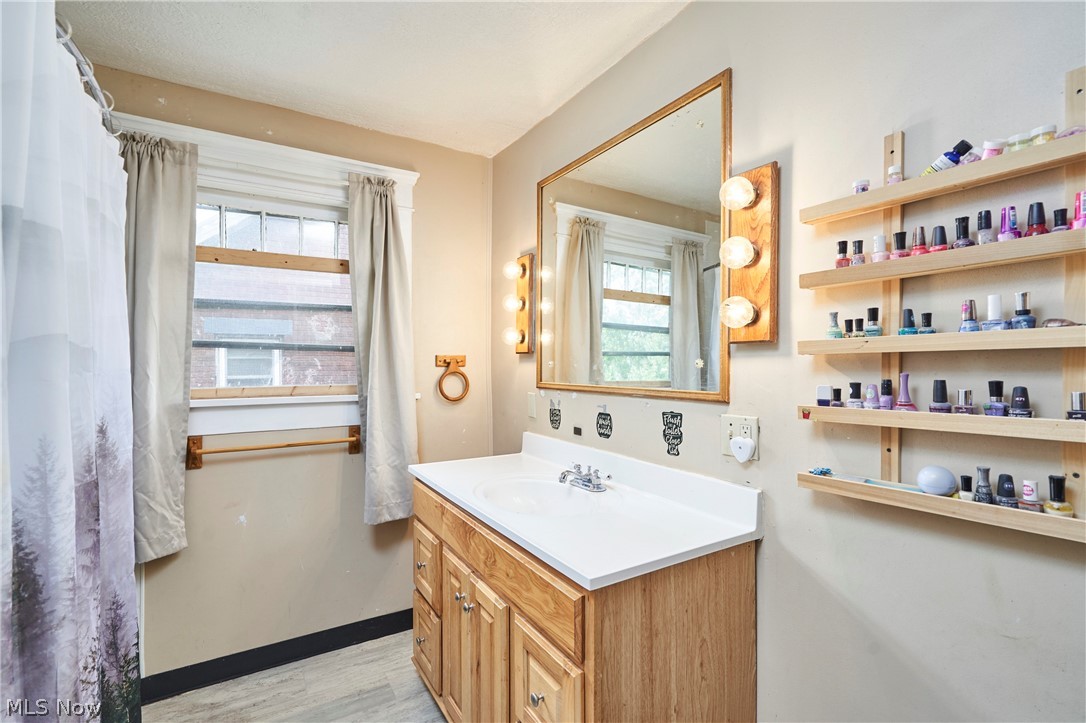 136 Smith Avenue Northwest Canton, OH 44708 - Photo 5 of 19 Bathroom featuring a single vanity with a white countertop, wood-finish cabinetry, a large mirrored vanity, and wall-mounted vanity lighting