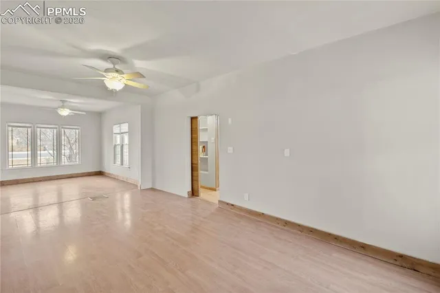 a view of an empty room with chandelier fan and wooden floor