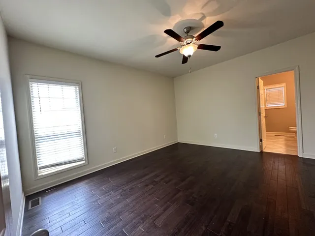 an empty room with wooden floor fan and windows