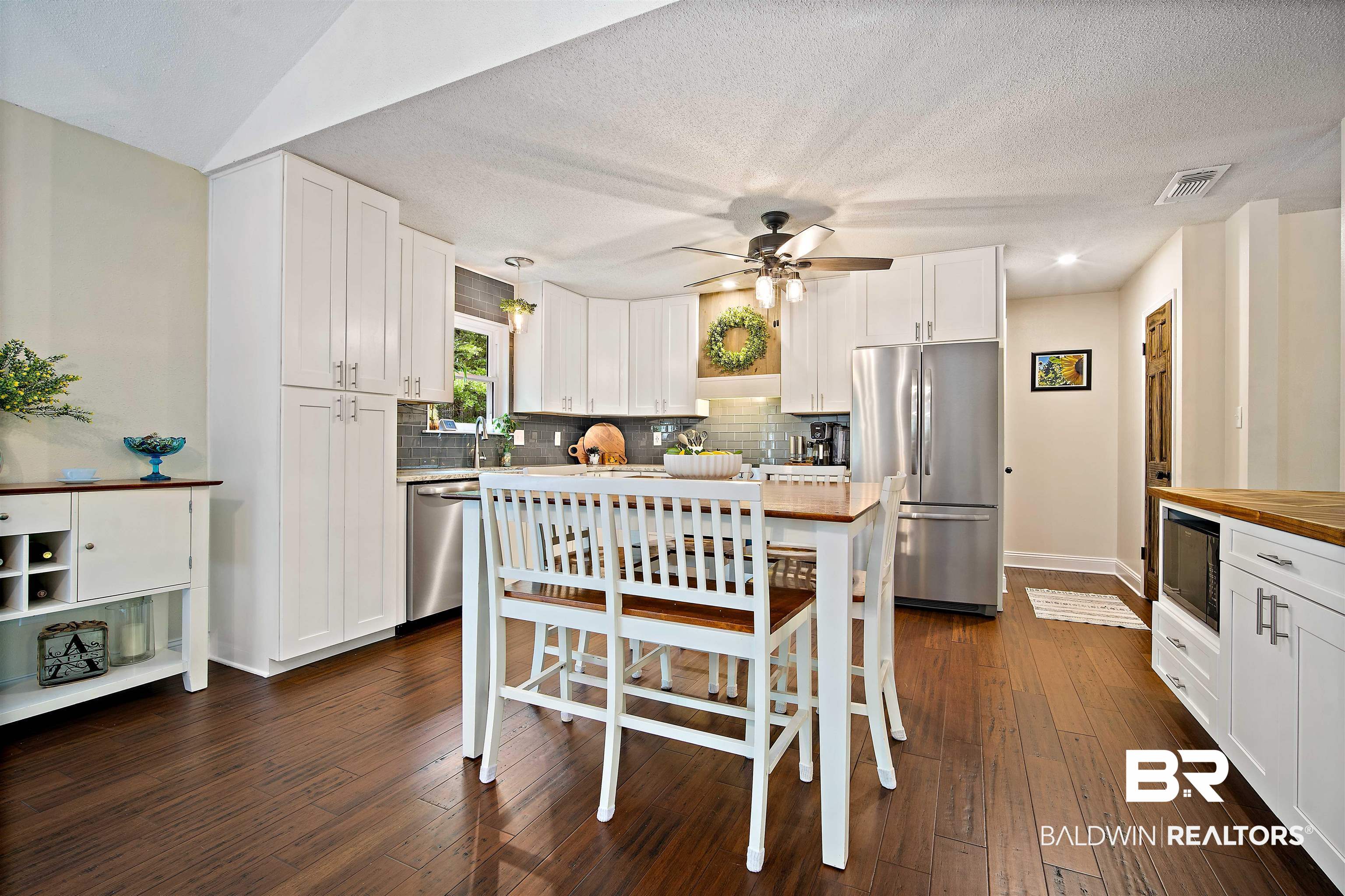71 Caisson Trace Daphne, AL 36527 - Photo 13 of 36 Renovated kitchen featuring wood-finish flooring, white cabinetry with contemporary hardware, a gray tiled backsplash, and stainless steel appliances including a refrigerator and built-in dishwasher
