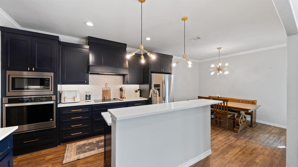 101 Lighthouse Lane Mabank, TX 75143 - Photo 9 of 40 Kitchen with ornamental molding, stainless steel appliances, backsplash, a center island with sink, and dark wood-style flooring