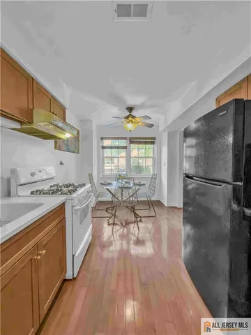 a kitchen with stainless steel appliances a stove a sink dishwasher a refrigerator white cabinets and wooden floor