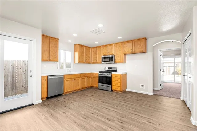 a kitchen with stainless steel appliances granite countertop wooden cabinets a sink a stove a refrigerator and microwave with wooden floor