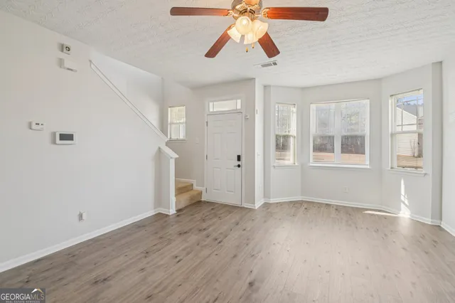 an empty room with wooden floor chandelier fan and windows