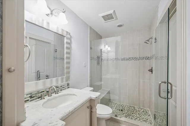 a bathroom with a granite countertop sink a mirror a toilet and shower